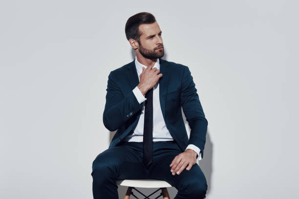 istock Tired. Handsome young man pulling his collar while sitting against grey background 1155179386