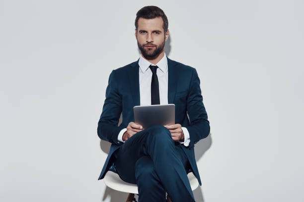 istock Confident businessman. Handsome young man working using digital tablet and looking at camera while sitting against grey background 1155179476