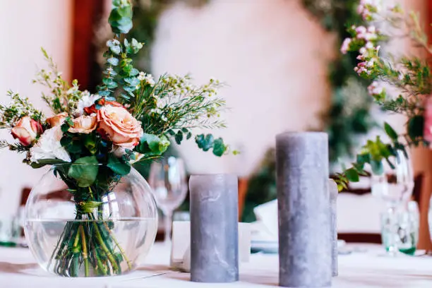 Bouquet of roses and greenery stands in a glass vase stands among black candles  in the middle of dinner table