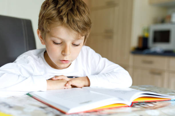 istock Little blonde school kid boy reading a book at home 1155181175