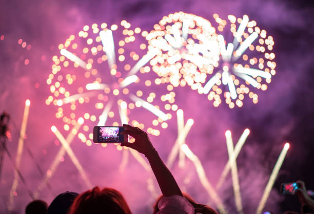 Raised hand with shooting horizontal night fireworks sky video smartphone . Colorful bright background entertainment with light and laser show. Raised hand with shooting horizontal night fireworks sky video smartphone . Colorful bright background entertainment with light and laser show. firework display photos stock pictures, royalty-free photos & images