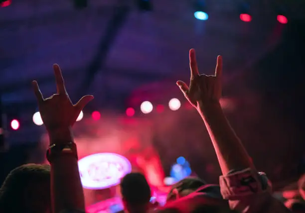 Photo of Young teenager girl raised up two hands with sign of the horns gesture supporting favorite rock band on the night concert