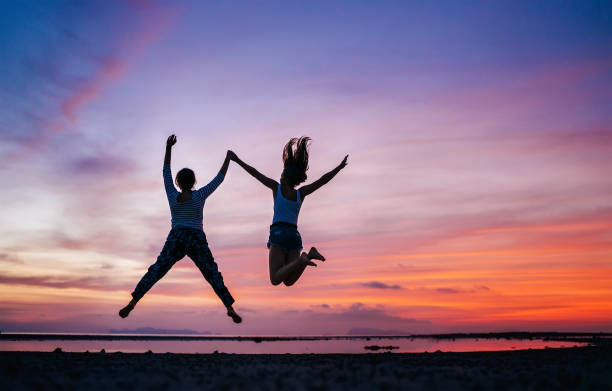 istock Two running and jumping girlfriends on the sunset sea beach. Hand in hand concept image. 1155183257