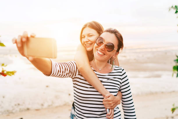 istock Two caucasian girlfriends hugging and posing for selfie on the sea side using smartphone. Careless vacation time concept image. 1155183266