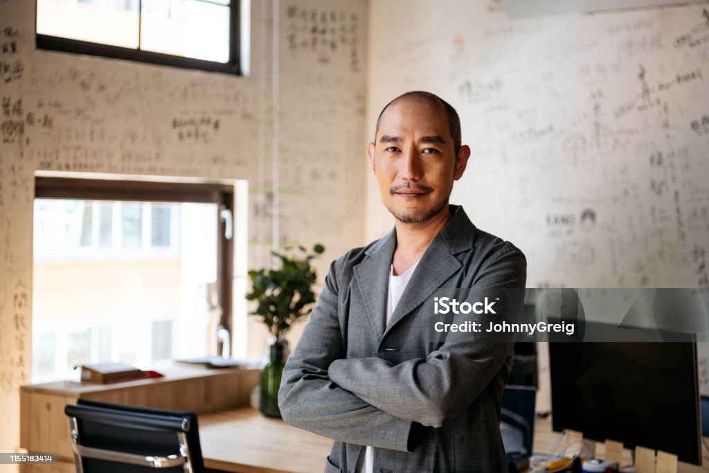 Portrait of Chinese businessman in creative office Man in 50s with arms crossed smiling towards camera with contented expression, executive, manager, confidence Asian and Indian Ethnicities Stock Photo