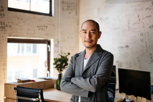 Man in 50s with arms crossed smiling towards camera with contented expression, executive, manager, confidence