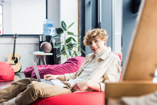 istock handsome casual businessman sitting in bean bag chair and looking at camera while using laptop in loft office 1155183861