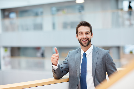 Portrait of a young businessman showing thumbs up in an office