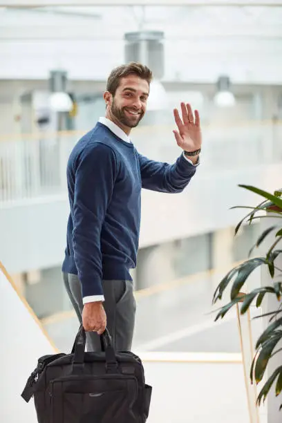 Portrait of a young businessman waving while carrying a bag