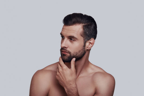 istock Time to shave. Handsome young man touching his beard while standing against grey background 1155187716