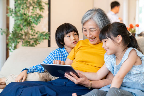 grandmother with her grandchildren looking at a digital tablet - wireless technology cheerful granddaughter grandmother imagens e fotografias de stock