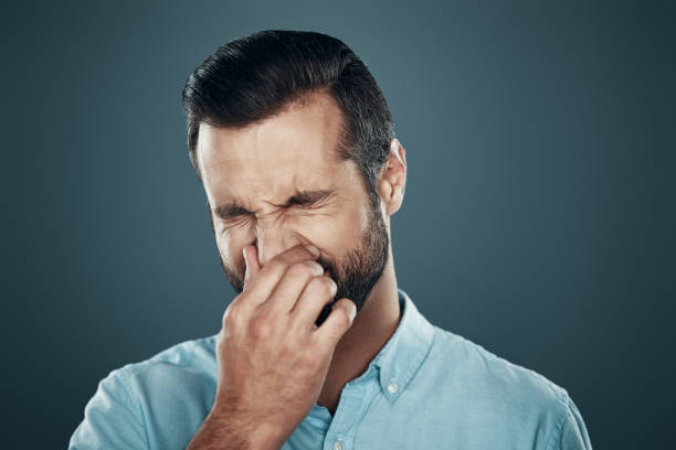 Allergy. Handsome young man covering nose with hand while standing against grey background Allergy. Handsome young man covering nose with hand while standing against grey background holding nose stock pictures, royalty-free photos & images