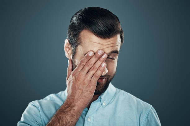 istock Feeling tired. Handsome young man covering eye with hand and smiling while standing against grey background 1155191101