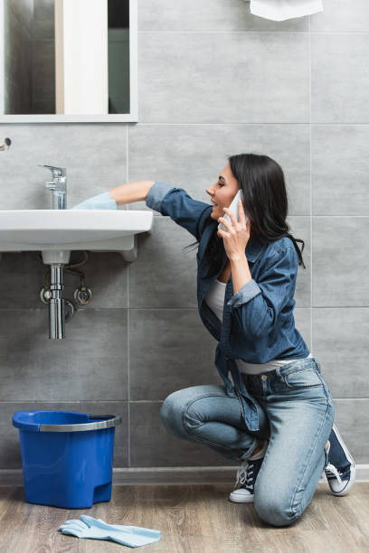istock Smiling woman talking on phone while repairing faucet 1155196049