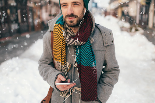 Young man listening music on the headset while walking on a snowy day