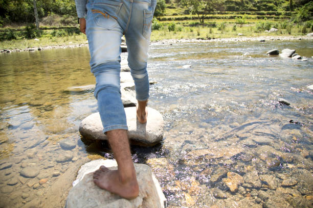homme traversant une rivière - stepping stone stone stepping footpath photos et images de collection