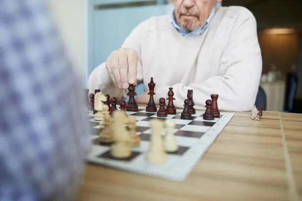 Aged experienced professional grandmaster with grey beard playing chess with opponent in checked shirt