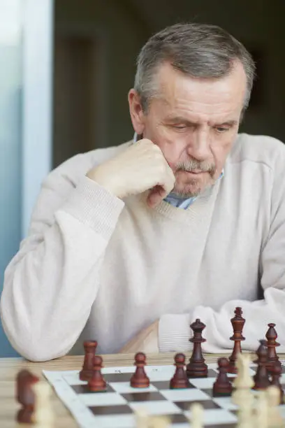 Puzzled old experienced grandmaster with wrinkled forehead and grey beard carefully thinking about next chess move