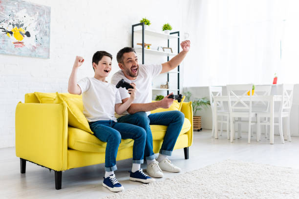 istock excited father and son cheering while playing Video Game on couch at home 1155210537