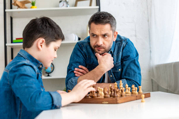 istock handsome father and son in denim playing chess while sitting at table at home 1155210729