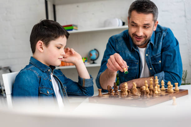 istock selective focus of father and son in denim playing chess while sitting at table at home 1155210743