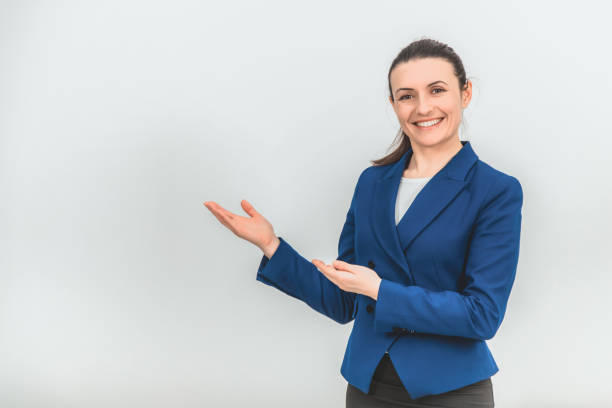 istock Young beautiful teacher standing, pointing at the copy space for text or product on her side, smiling. 1155212793