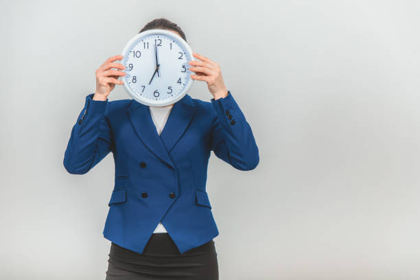 istock Funny young teacher in formal suit hiding her face behind a white clock. 1155213581