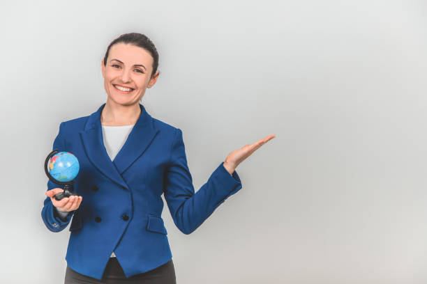 istock Beautiful young geography teacher with globe in one hand, pointing at the copyspace for text or product on the side, smiling. 1155213874