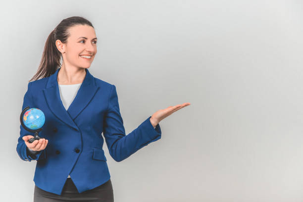 istock Beautiful young geography teacher with globe in one hand, pointing at the copyspace for text or product on the side, smiling. 1155214083