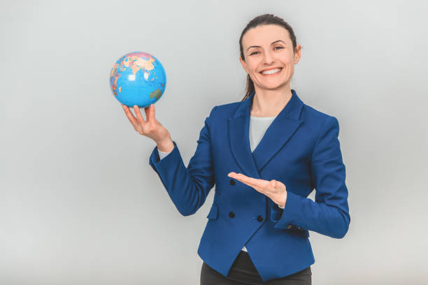 istock Young geography teacher holding a globe, pointing her hand at it, smiling. 1155214174