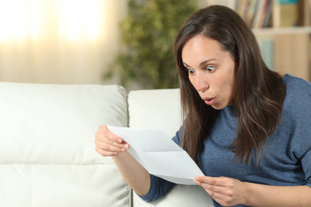 istock Surprised woman reading a letter on a couch at home 1155214643