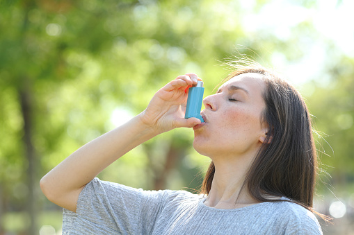 Woman is using an asthma inhaler in a park