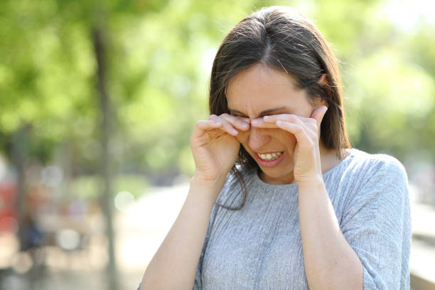 una mujer disgustada frotándose los ojos en un parque - ojo humano fotografías e imágenes de stock