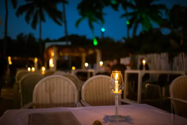 Photo of Dinner table ready with candle lights in a white stand for evening service at a beach shack restaurant.