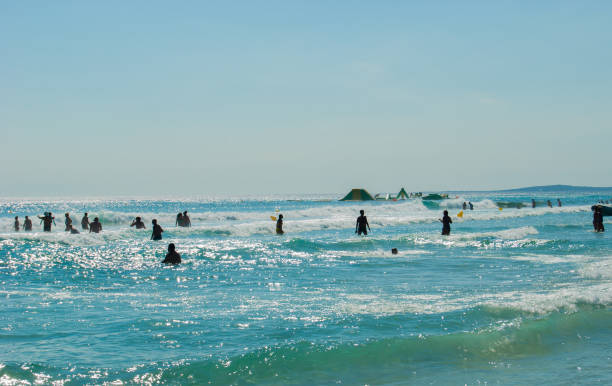 Black silhouettes of people enjoying the rough and blue sea during a sunny day in the summer