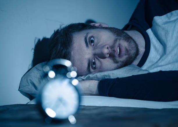 istock Insomnia Stress and Sleeping disorder concept. Sleepless desperate young caucasian man awake at night not able to sleep, feeling frustrated and worried looking stressed and concerned at alarm clock. 1155221202
