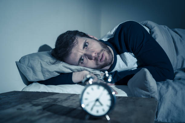 istock Insomnia Stress and Sleeping disorder concept. Sleepless desperate young caucasian man awake at night not able to sleep, feeling frustrated and worried looking stressed and concerned at alarm clock. 1155221249