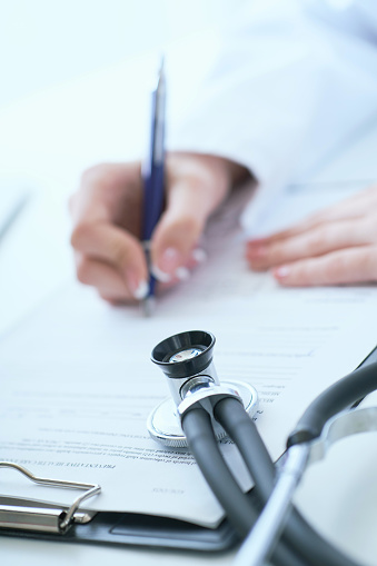 Female medicine doctor hand holding silver pen writing something on clipboard closeup. Medical care, insurance, prescription, paper work or career concept. Physician examining patient.