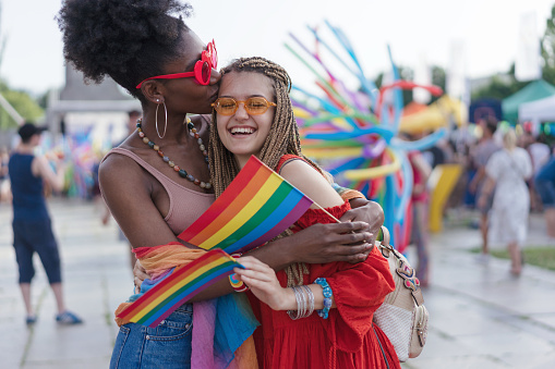 Lovely young women waving rainbow pride flags, hugging and kissing