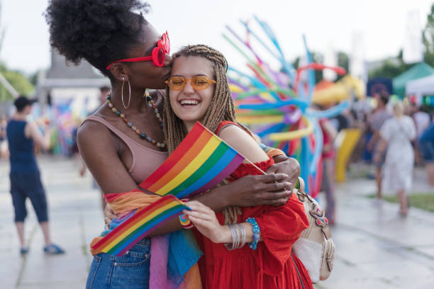 Young women hugging and kissing at the love parade Lovely young women waving rainbow pride flags, hugging and kissing gender stereotypes photos stock pictures, royalty-free photos & images
