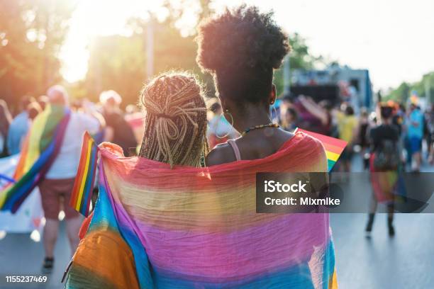 Young Female Couple Hugging With Rainbow Scarf At The Pride Event Stock Photo - Download Image Now