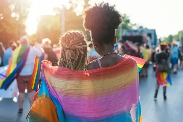 Rear view image of young couple walking with the pride event, hugging and waving pride flags