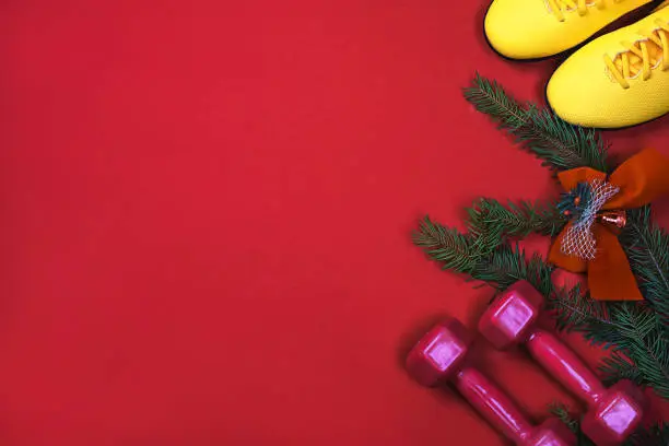 Photo of Exercise, Fitness, sport and Working Out Merry Christmas and Happy new year background with dumbbells, yellows sneakers, branches fir tree, holiday decorations on red background.