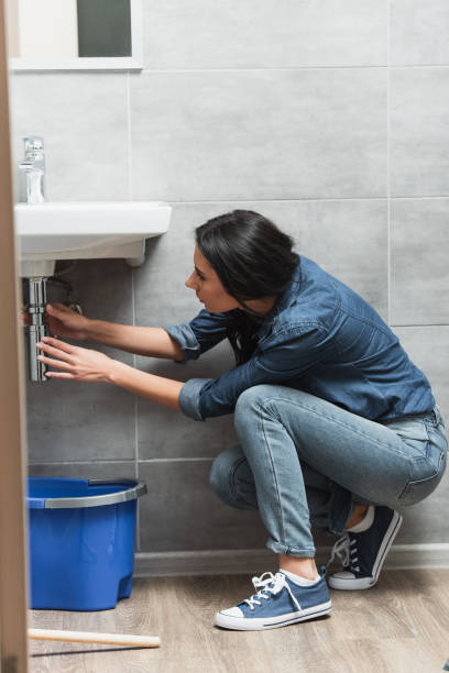 istock Brunette woman in jeans fixing pipe in bathroom 1155239445