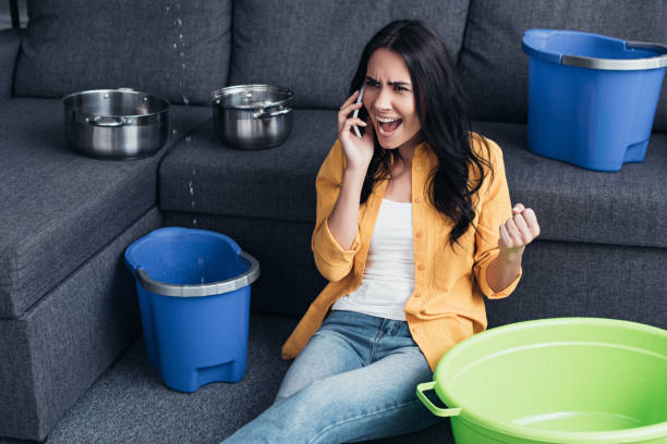 istock Aggressive woman talking on smartphone and sitting on floor under leaking ceiling 1155239480