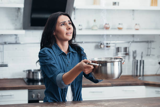 istock Stressed young woman using steel pot during water leak in kitchen 1155239628