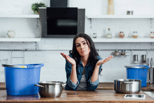 istock Brunette woman using pots and buckets during leak in kitchen 1155239664