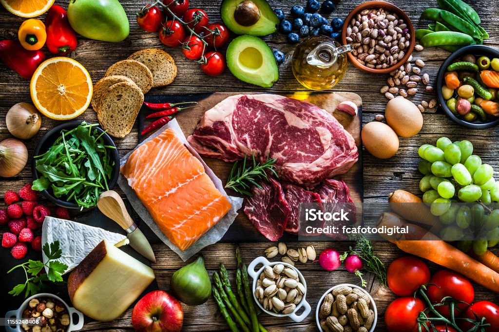 Food backgrounds: table filled with large variety of food Food backgrounds: top view of a rustic wooden table filled with different types of food. At the center of the frame is a cutting board with beef steak and a salmon fillet and all around it is a large variety of food like fruits, vegetables, cheese, bread, eggs, legumes, olive oil and nuts. DSRL studio photo taken with Canon EOS 5D Mk II and Canon EF 70-200mm f/2.8L IS II USM Telephoto Zoom Lens Food Stock Photo