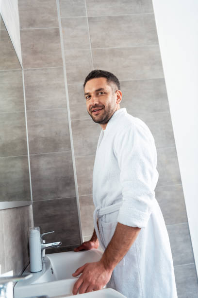 istock handsome smiling man in white bathrobe looking at camera in bathroom during morning routine 1155240428
