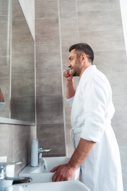 istock handsome man in white bathrobe brushing teeth in bathroom during morning routine 1155240444